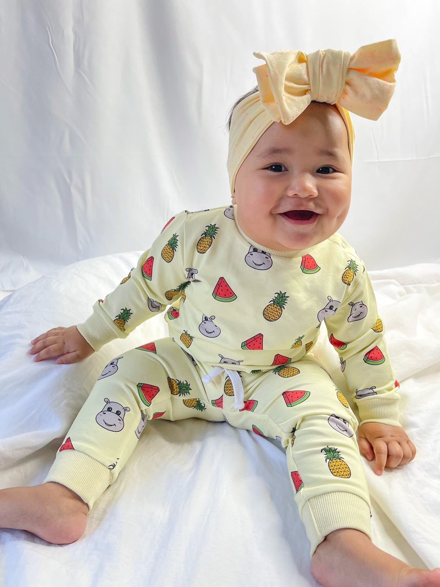 baby girl sitting down wearing pineapple and watermelon hungry hippo print baby lounge set