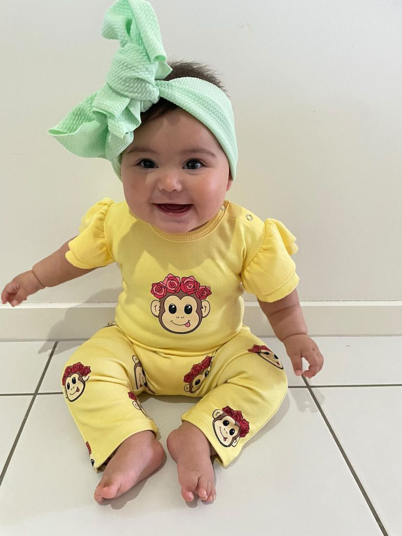 Baby girl sitting down and smiling. Wearing a yellow romper and yellow pants with a cute monkey print on it
