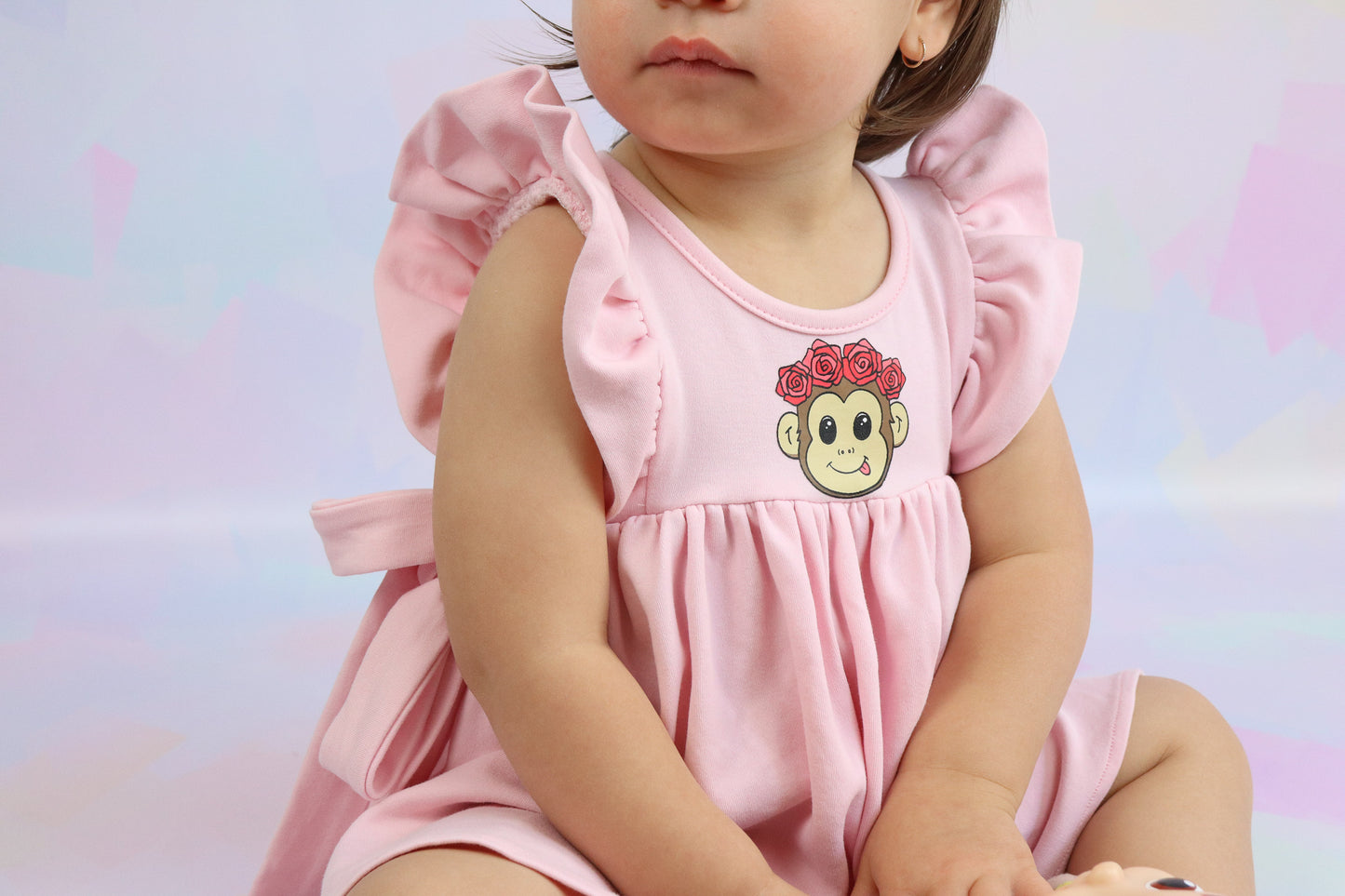 toddler girl sitting down wearing a pastel pink dress with a cute monkey face printed on it
