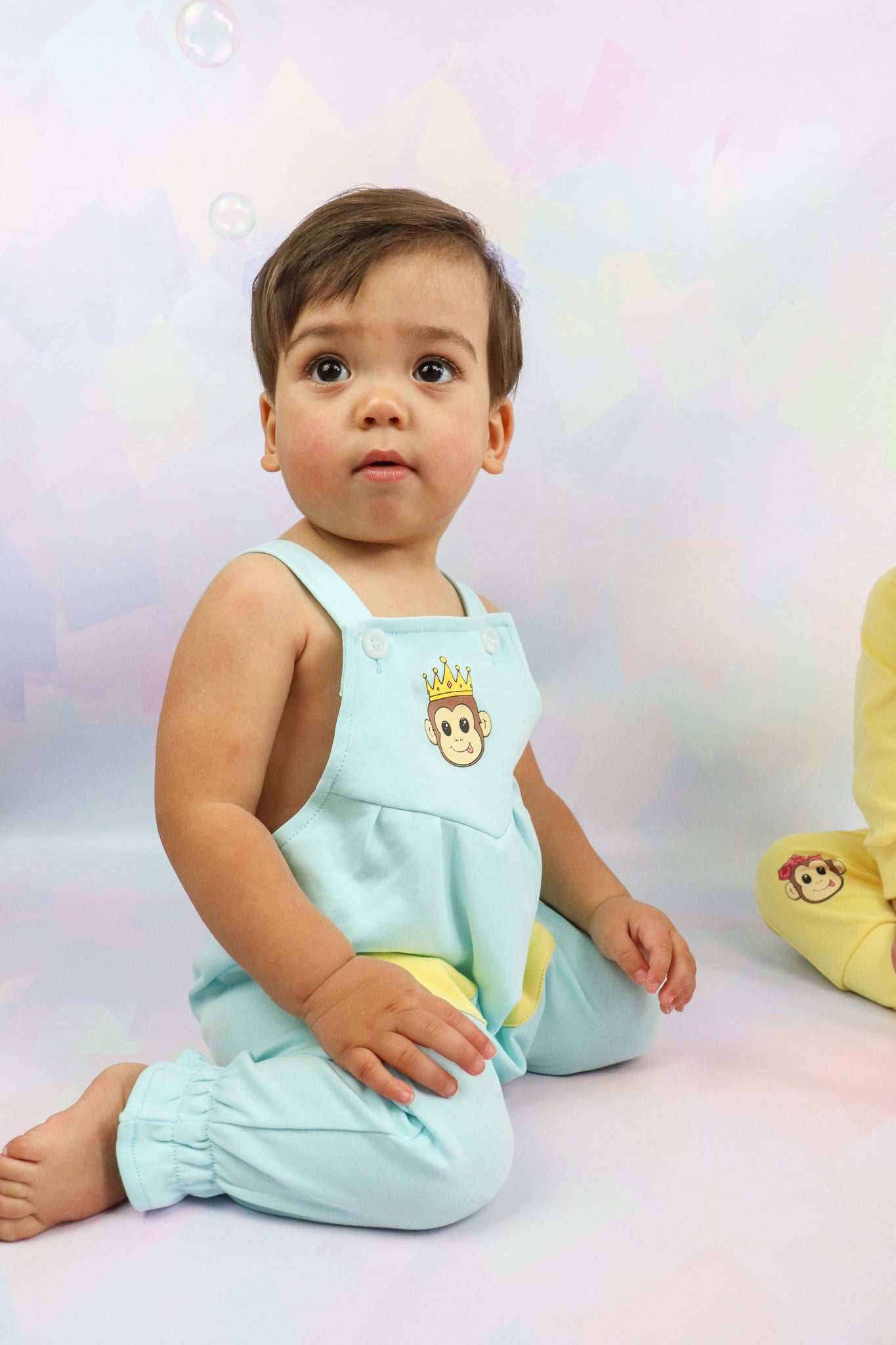 toddler boy sitting down wearing pastel blue overalls with a cute monkey design