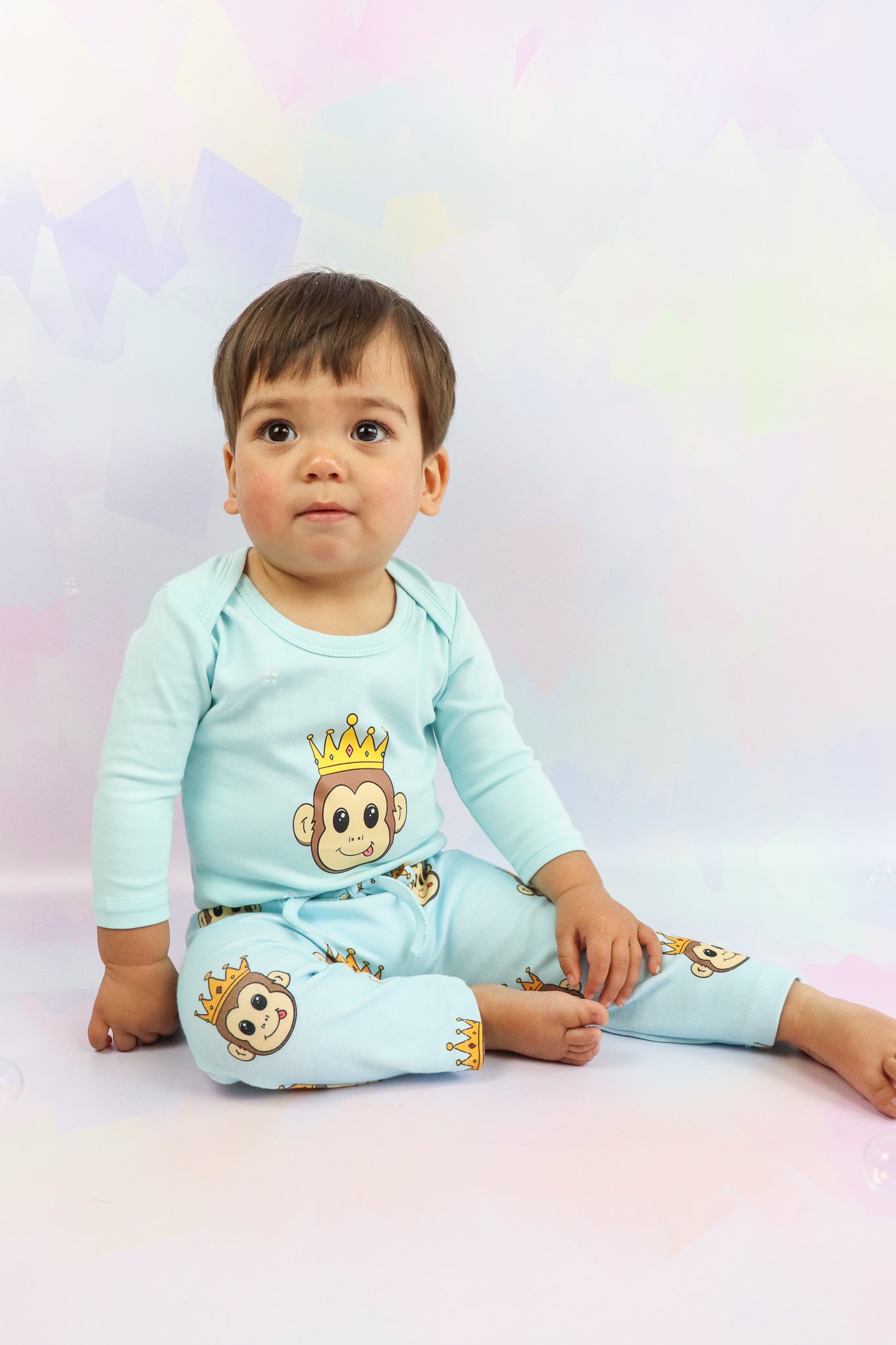 baby boy sitting down wearing pastel blue romper and pants with cute monkey design print