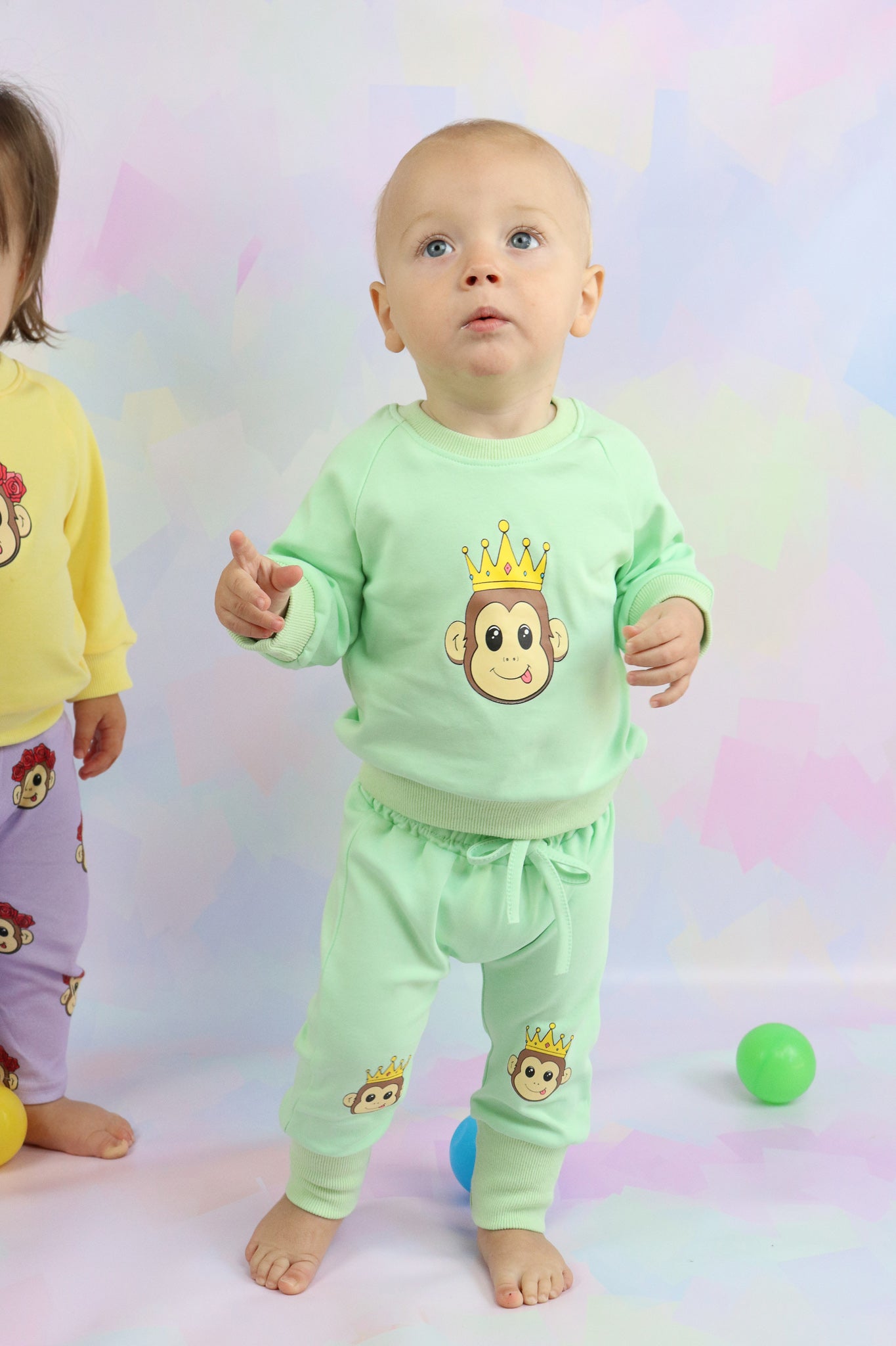 toddler boy standing up, wearing pastel green lounge set with cute monkey faces printed on it