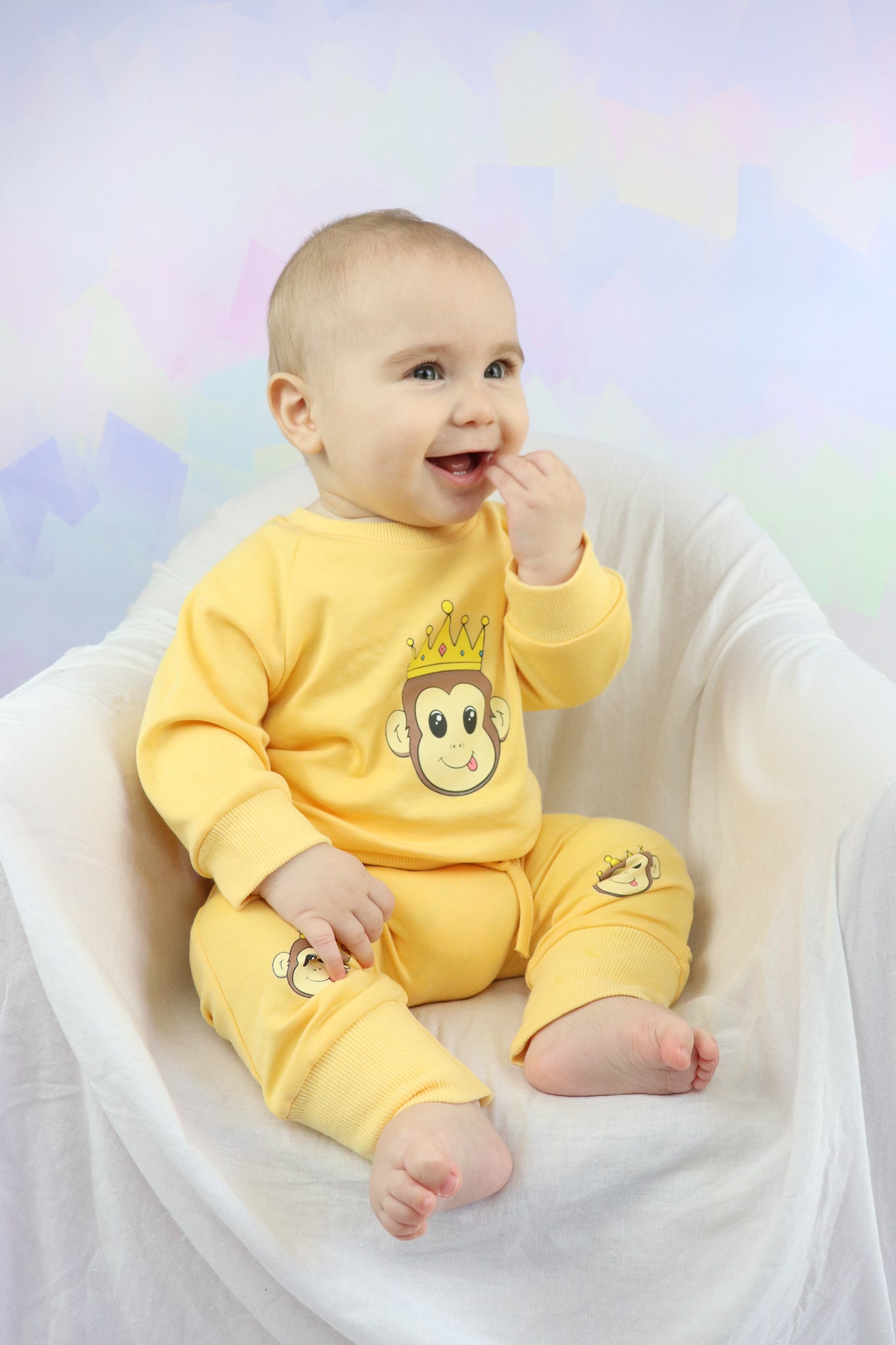 baby boy sitting down and smiling. Wearing a pastel orange lounge set with cute monkey faces printed on it