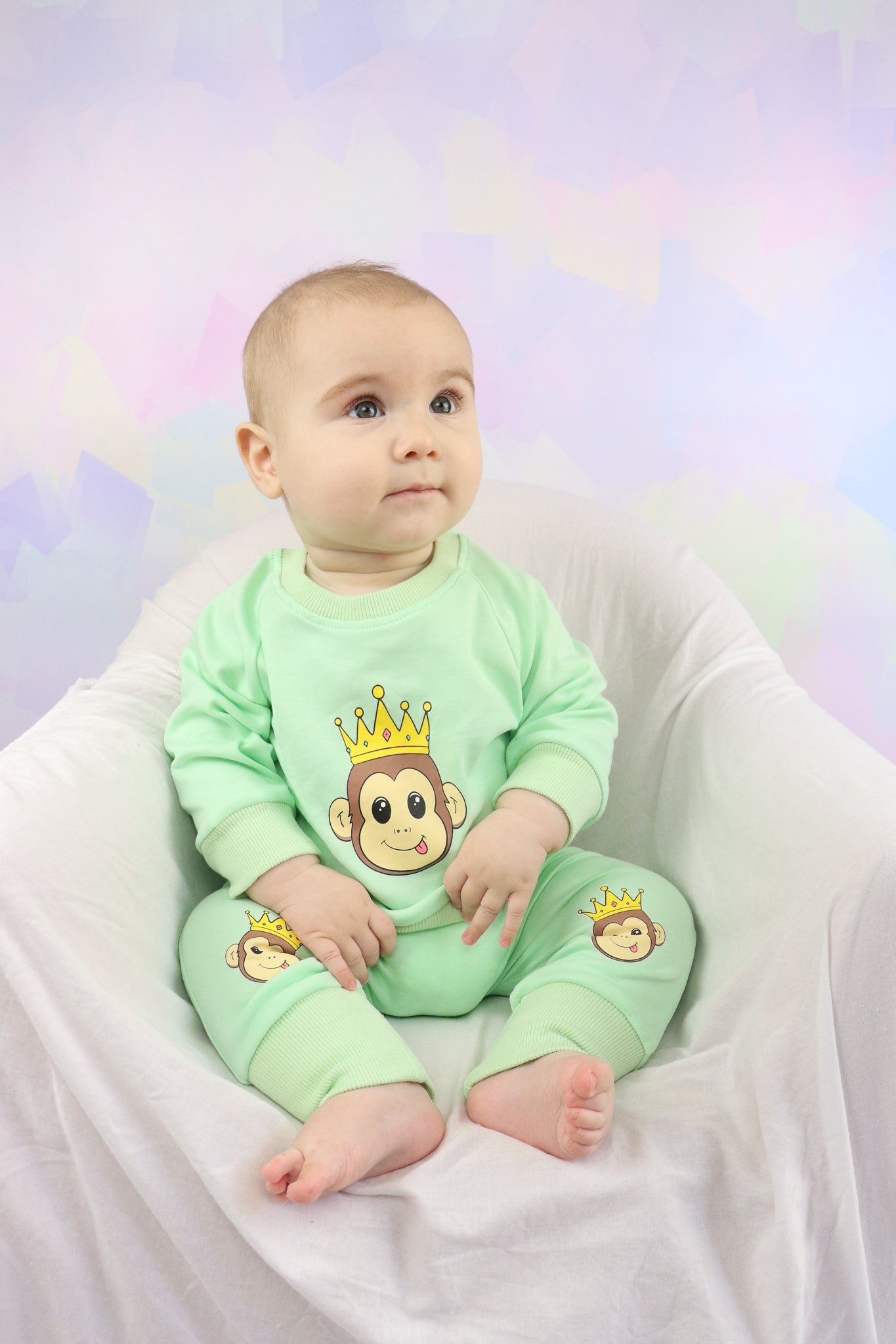 baby boy sitting on a chair wearing a pastel green outfit set with cute monkey faces printed on it