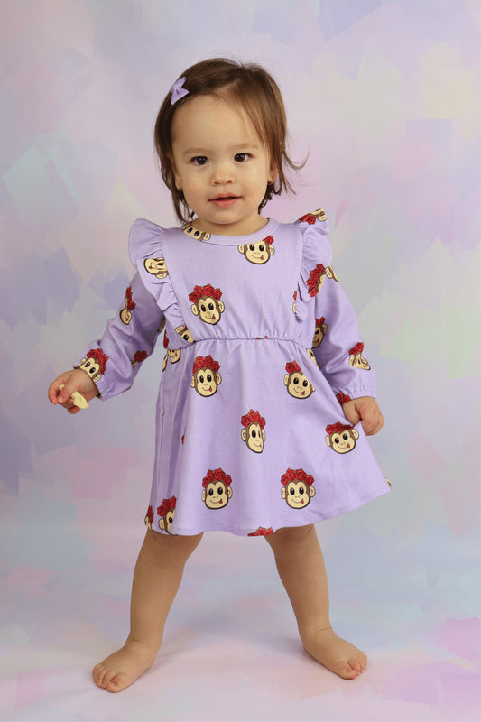 toddler girl wearing a pastel purple long sleeve dress with frill shoulders. Cute monkey faces printed all over