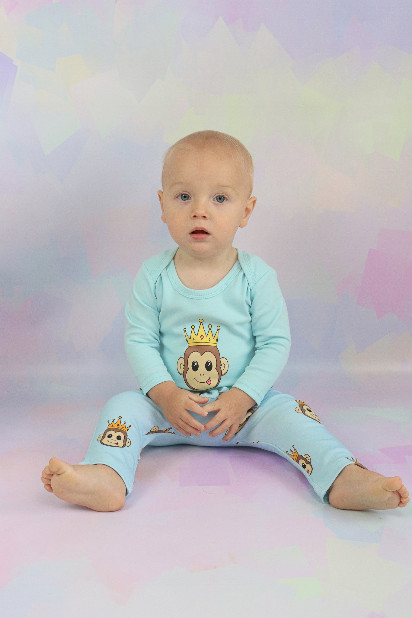 Baby boy sitting down wearing a pastel blue long sleeve romper with a cute monkey design on it. Also wearing pants with the cute monkey design all over