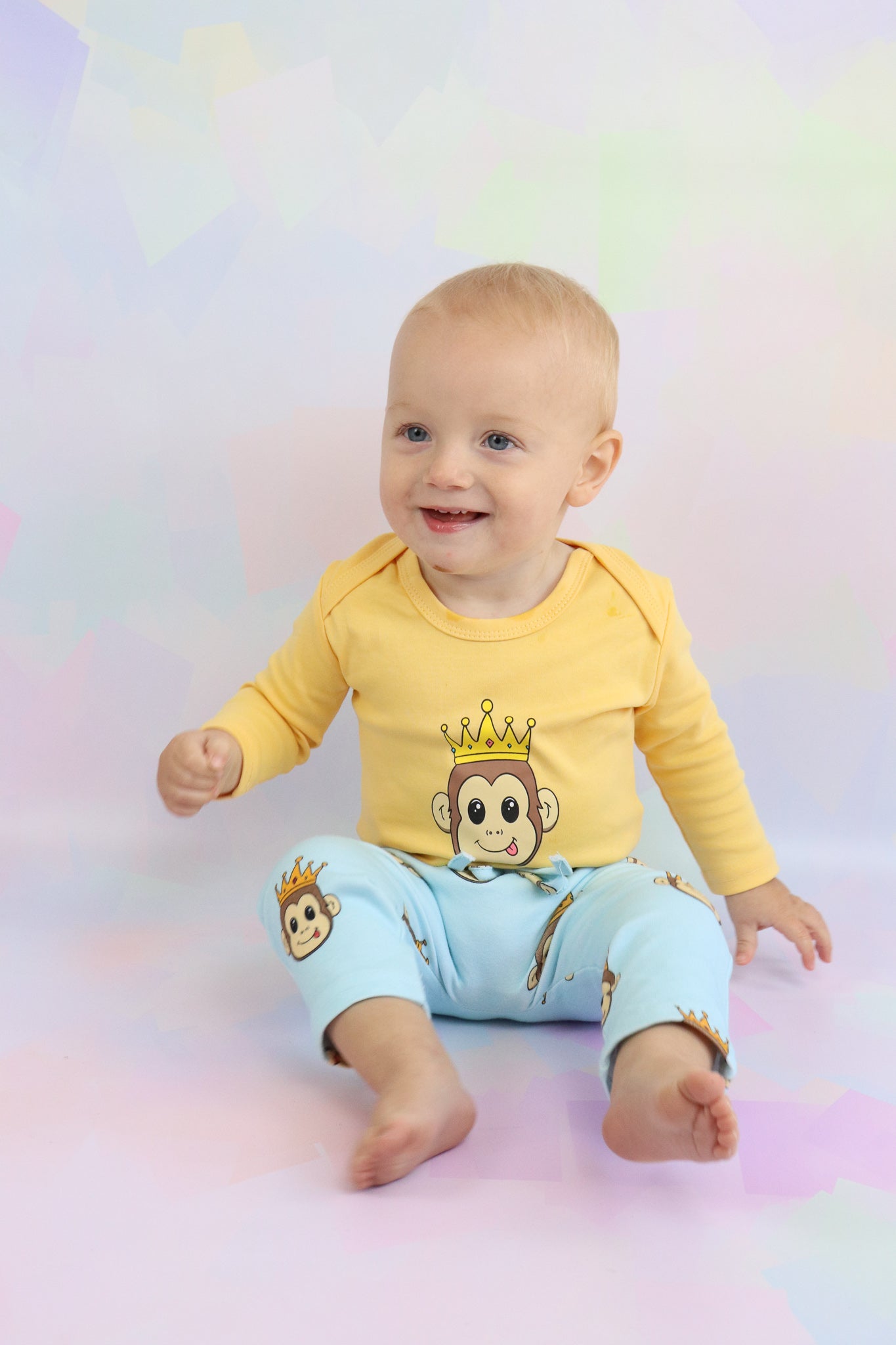 toddler boy sitting down smiling and wearing a pastel orange long sleeve romper. Paired with pastel blue pants with a cute monkey design printed all over