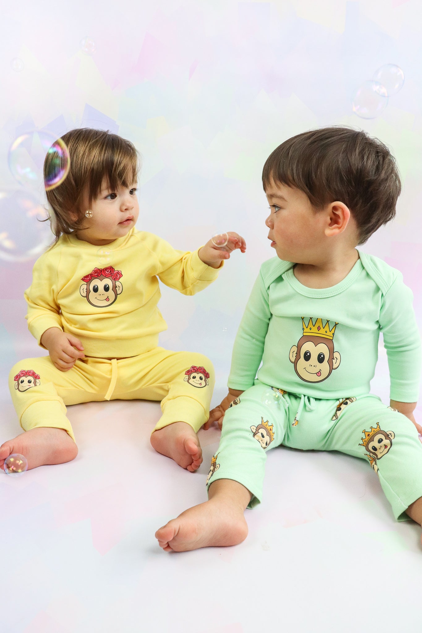 2 toddlers sitting down wearing colourful baby clothes with a cute monkey design print