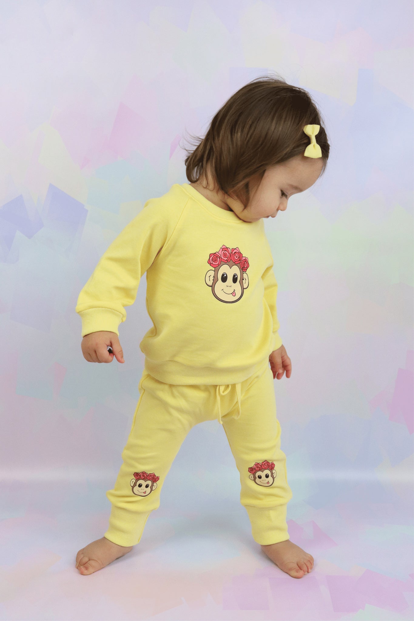 toddler girl wearing a pastel yellow lounge set with cute monkey faced printed on it